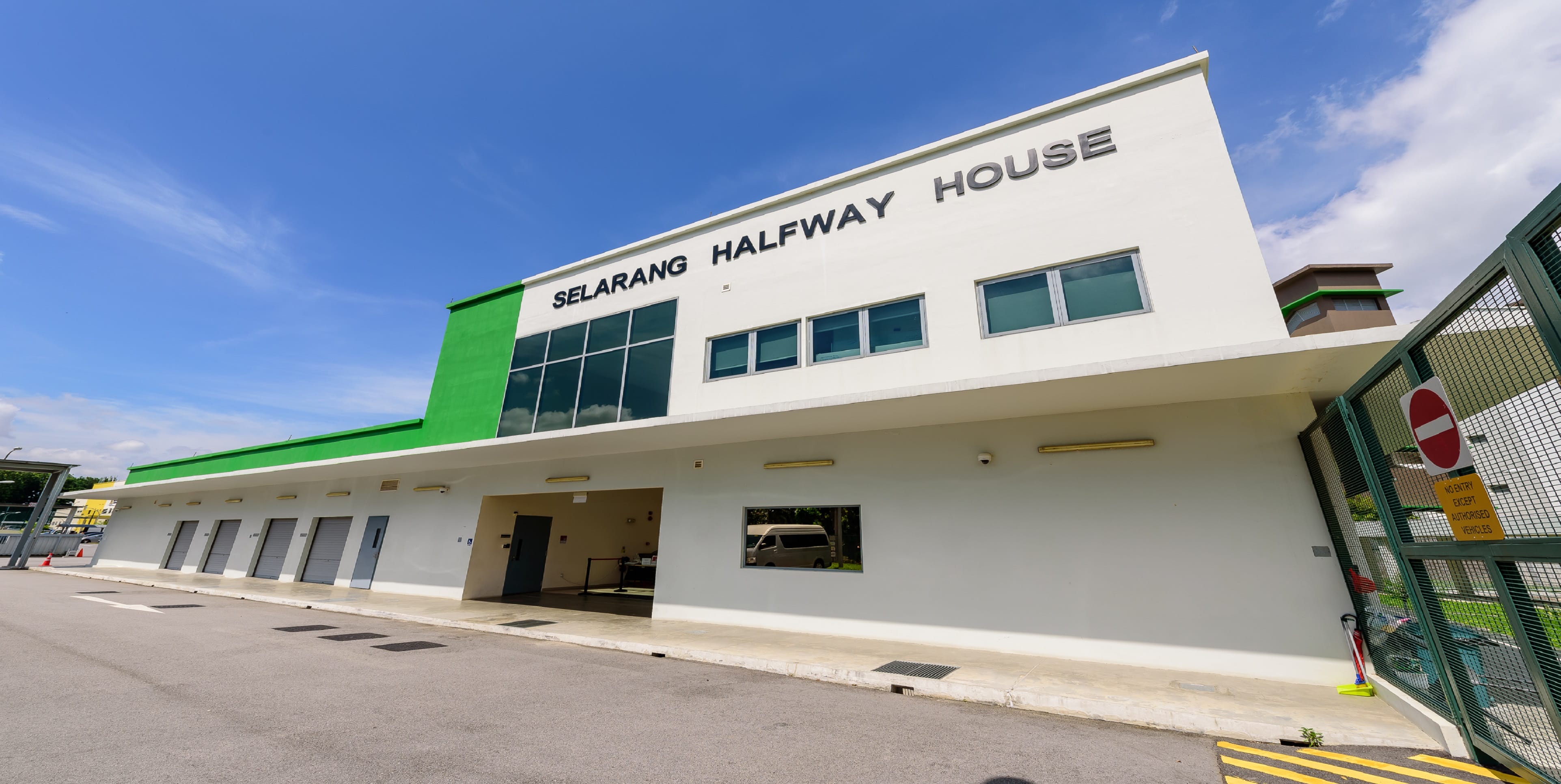 A building labeled "Selarang Halfway House" with a green facade and gated entrance under a clear blue sky.